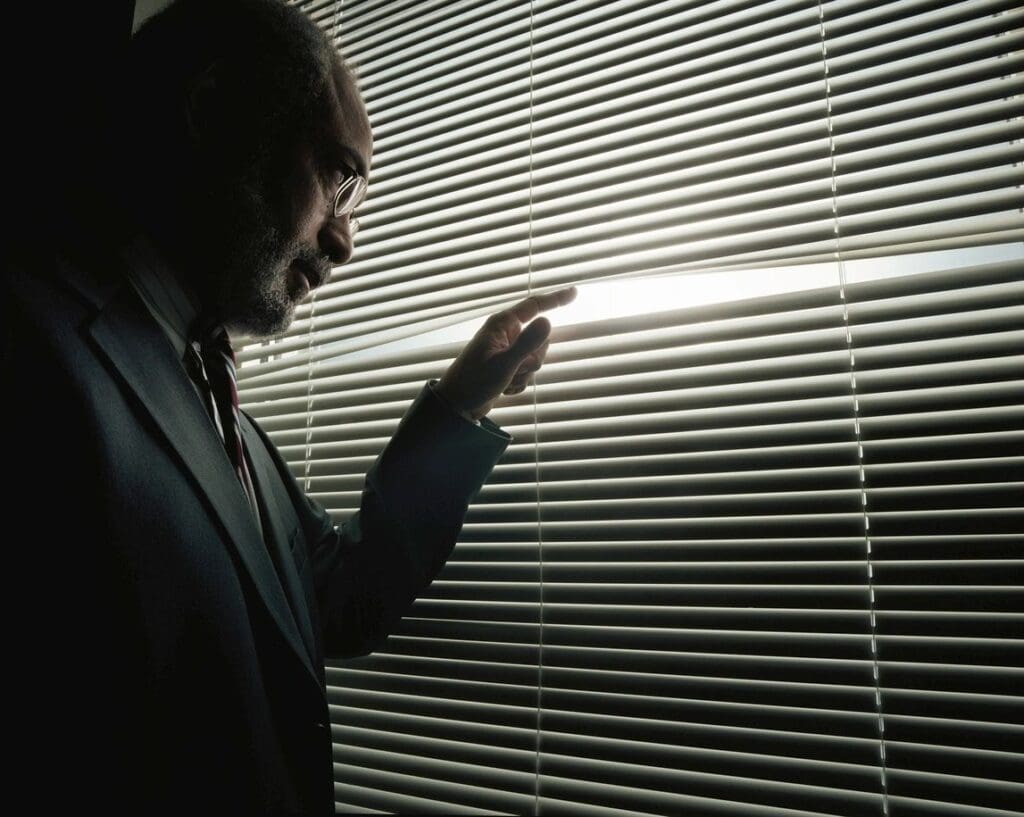 A man in suit looking out of blinds